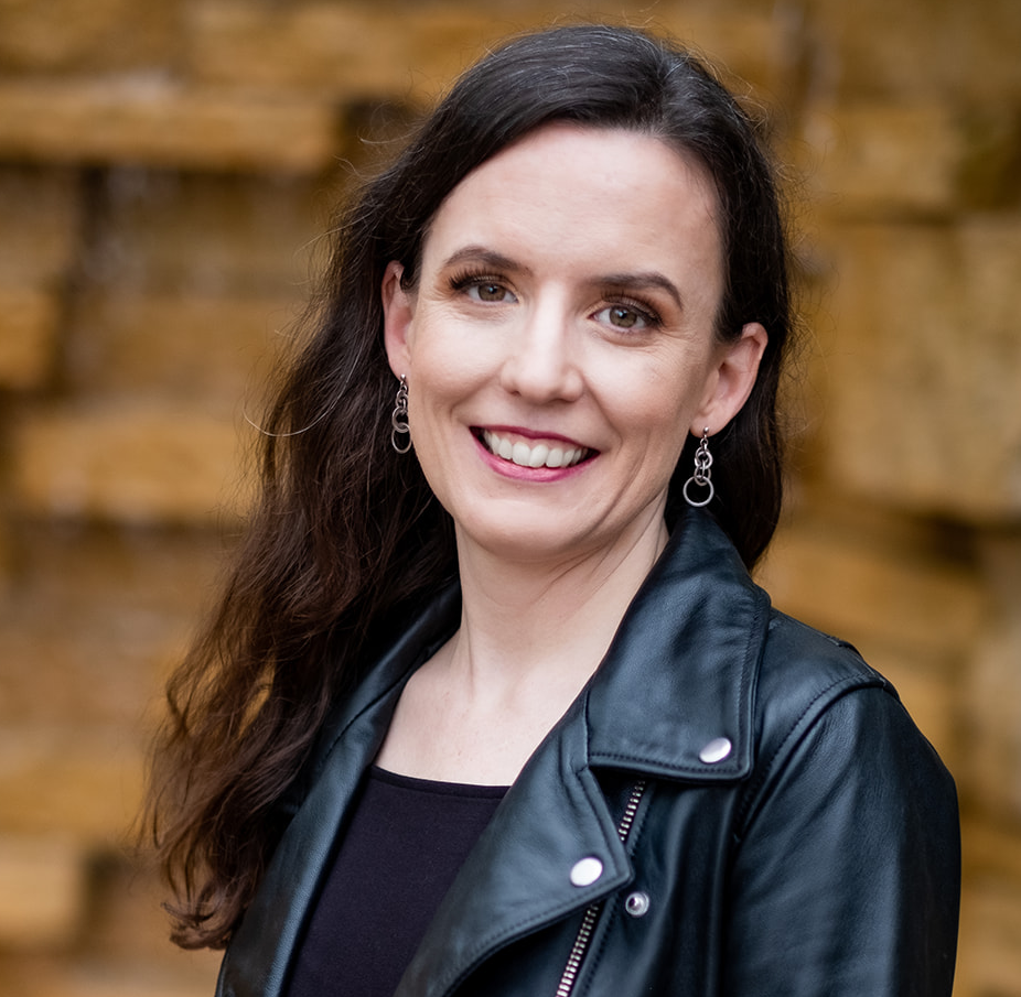 A headshot of a smiling woman in a black leather jacket. She has prominent earrings made of interlocking circles.